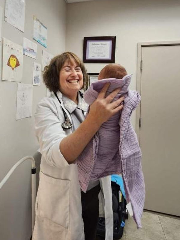 Natalia Pasumansky, DNP, smiling as she holds a newborn patient wrapped in a lavender blanket